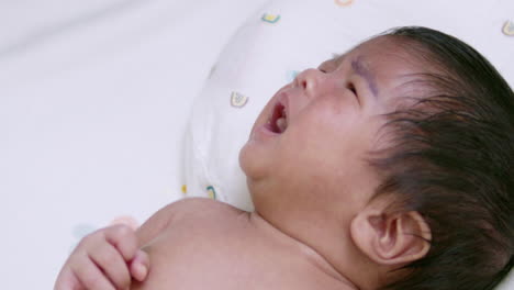 stretching while crying out loud, a newborn infant is screaming softly as it looks up to its parent while waiting to be cradled in its mother's arms