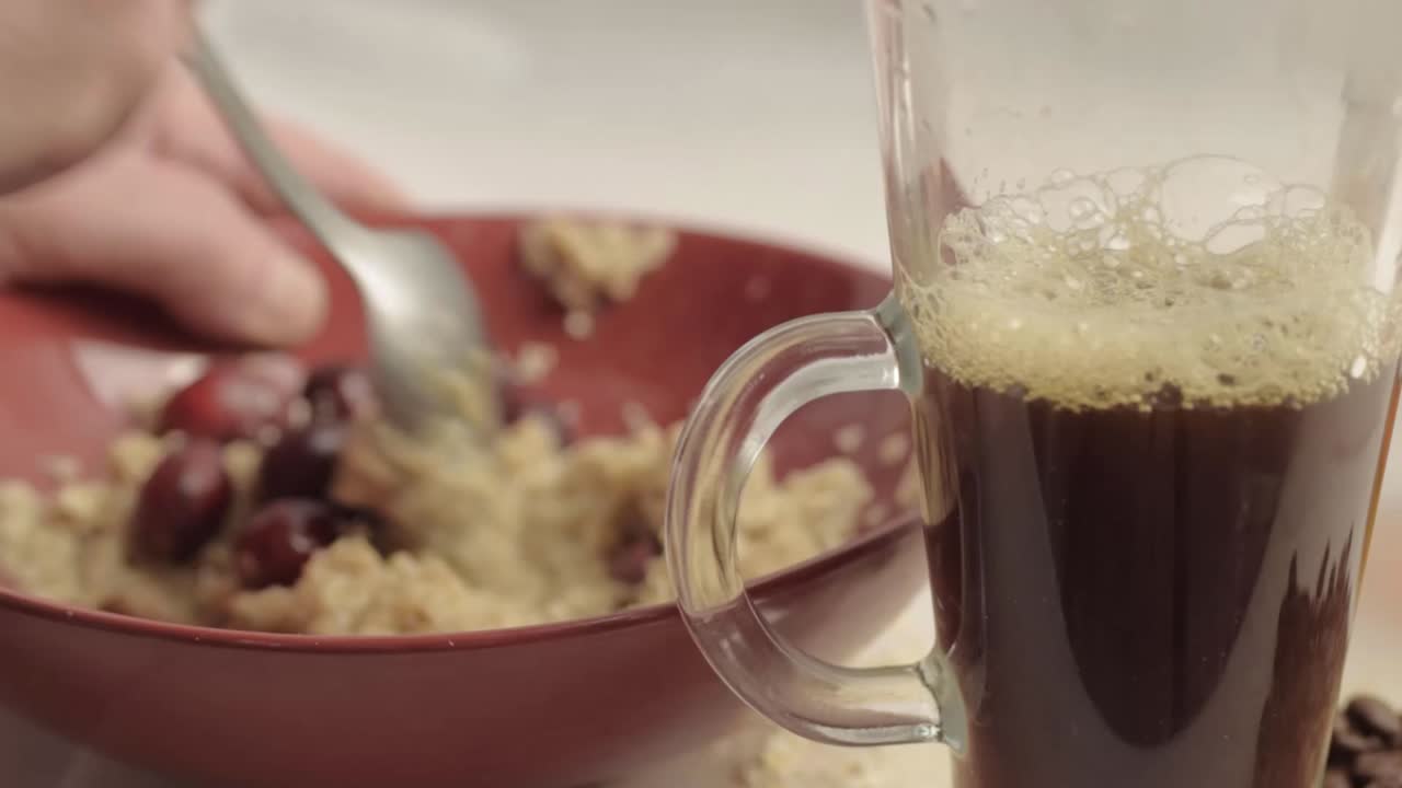 Hand eating breakfast of porridge, cranberries and fresh coffee