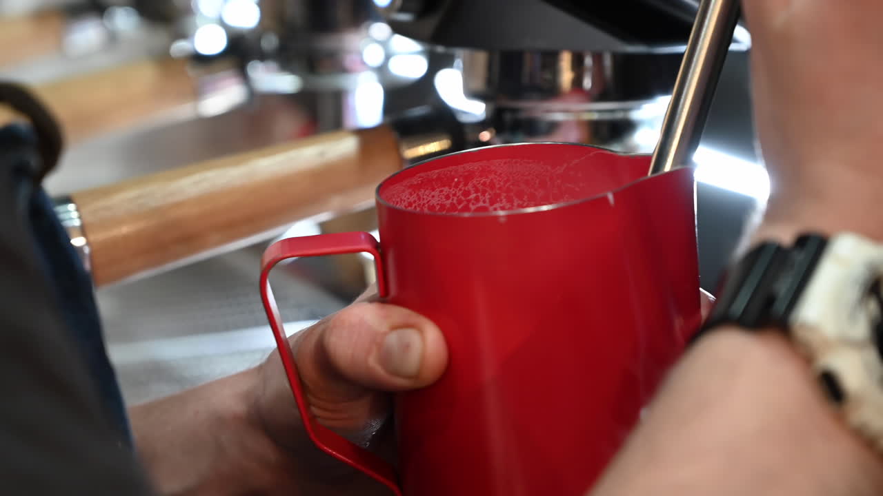 Close up of a barista making a coffee and frothing the milk at a cafe with a professional machine