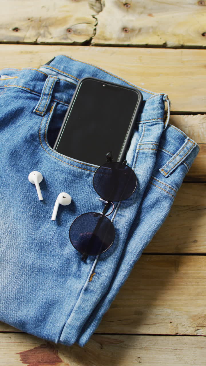 Vertical video of denim trousers with sunglasses, smartphone and earphones with copy space