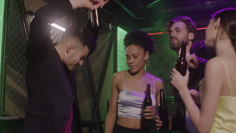 group of four young friends dancing and drinking beer at disco