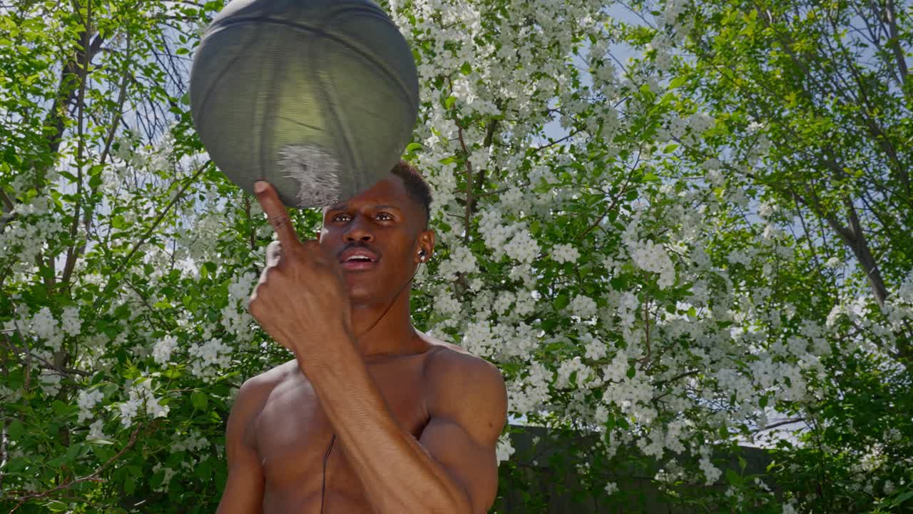 Giovane uomo che fa girare il pallone da basket sul dito all'aperto davanti a un albero in fiore