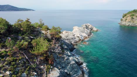 Drone-View-Over-A-Seaside-Cliff-With-Small-Isolated-Beaches,-Crystal-Clear-Water-And-Green-Vegetation-Near-Gramvousa-Island-,-Thassos-Island,-Greece,-Europe