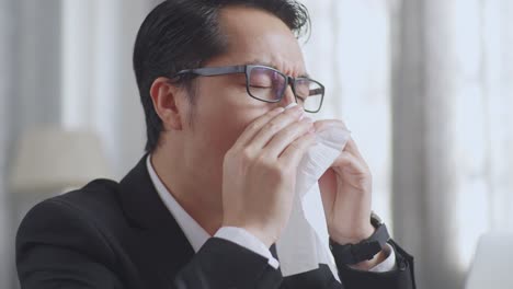 man blowing his nose at a computer