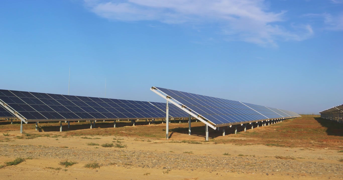 Rækker af solpaneler på en vedvarende energipark under en klar blå himmel med fotovoltaiske moduler i et tørt, åbent landskab, fanget i jævne videobilleder.