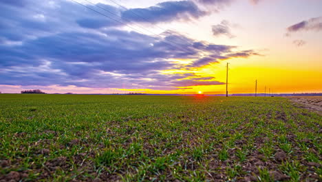 Amazing-cloudscape-in-timelapse-passing-over-farmland,-sun-setting-colorfully-in-orange-on-the-horizon-in-the-background