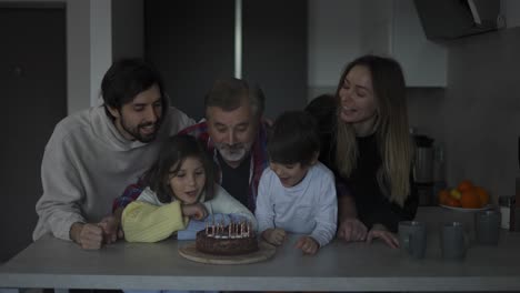 Abuelo-Feliz-Soplando-Velas-En-El-Pastel-De-Cumpleaños-Junto-Con-Su-Gran-Familia