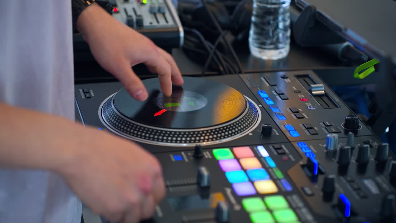 Primo piano della mano di un DJ professionista che scratcha un disco in vinile su un controller Pioneer CDJ nero con luci da spettacolo colorate e mixer in un set dal vivo in discoteca