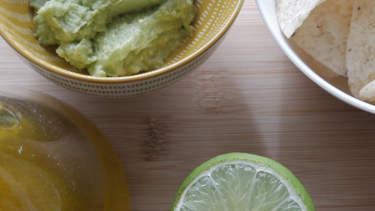 Fresh ingredients for guacamole, including lime, avocado mash, and olive oil in a bowl