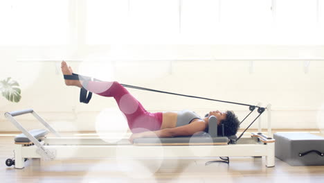 exercising on pilates reformer, woman stretching legs with resistance band