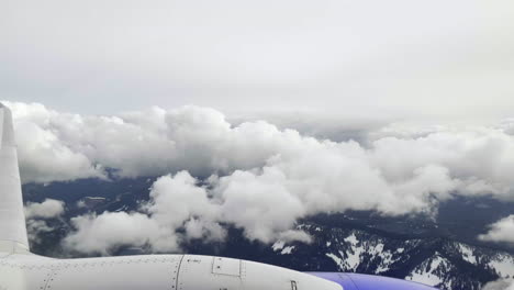 Punto-De-Vista-En-Primera-Persona-Desde-La-Ventana-De-Un-Avión-Mientras-Vuela-Sobre-Las-Montañas-Y-A-Través-De-Nubes-Blancas-E-Hinchadas