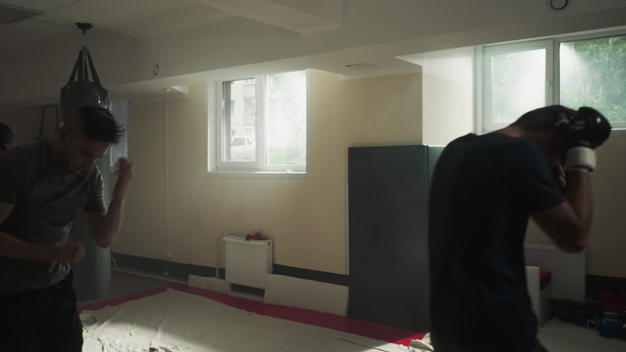 복싱 장비를 입은 전문 트레이너는 학생들에게 어두운 체육관에서 기본적인 전투 연습을 보여줍니다. 그룹 스포츠 활동과 멘토는 남성의 기술을 향상시니다.
