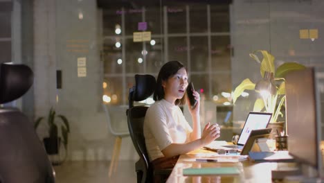 Happy-asian-casual-businesswoman-talking-on-smartphone-at-desk-in-office-at-night,-slow-motion