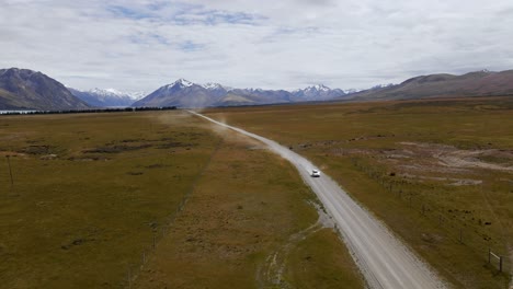 oncoming car on alpine dirt road between dry plains and snow-capped mountain range in background