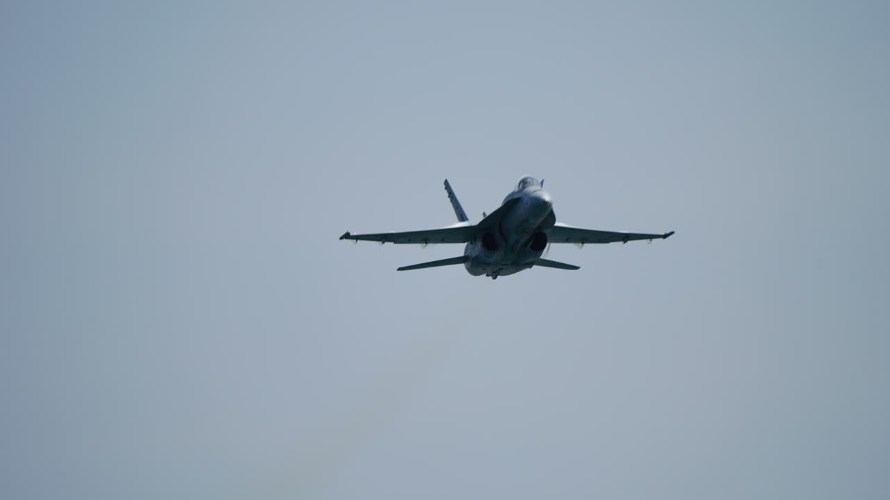Fighter jet soaring through clear blue sky, generating dramatic vapor trail while approaching camera in powerful slow motion shot, highlighting aerodynamic performance