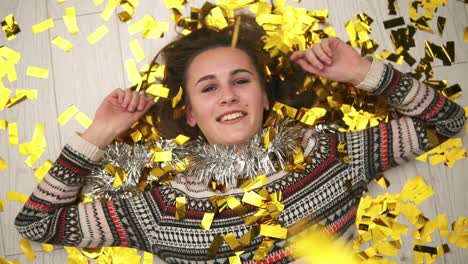 round camera movement: happy smiling girl lying on the floor, the golden confetti falling on her. slow motion shot