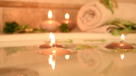 relajante fondo de spa con velas flotando en el agua del baño, algunos pétalos verdes y una toalla cerca de la superficie del agua