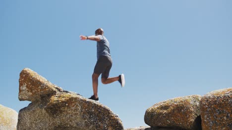 hombre afroamericano senior haciendo ejercicio corriendo sobre rocas junto al mar