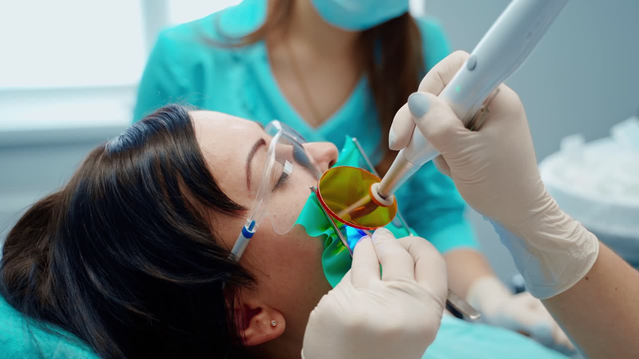 Dental treatment. Woman treats her teeth in clinic. Stomatologist's hands in gloves holding modern medical equipment in patient's mouth. Close-up.