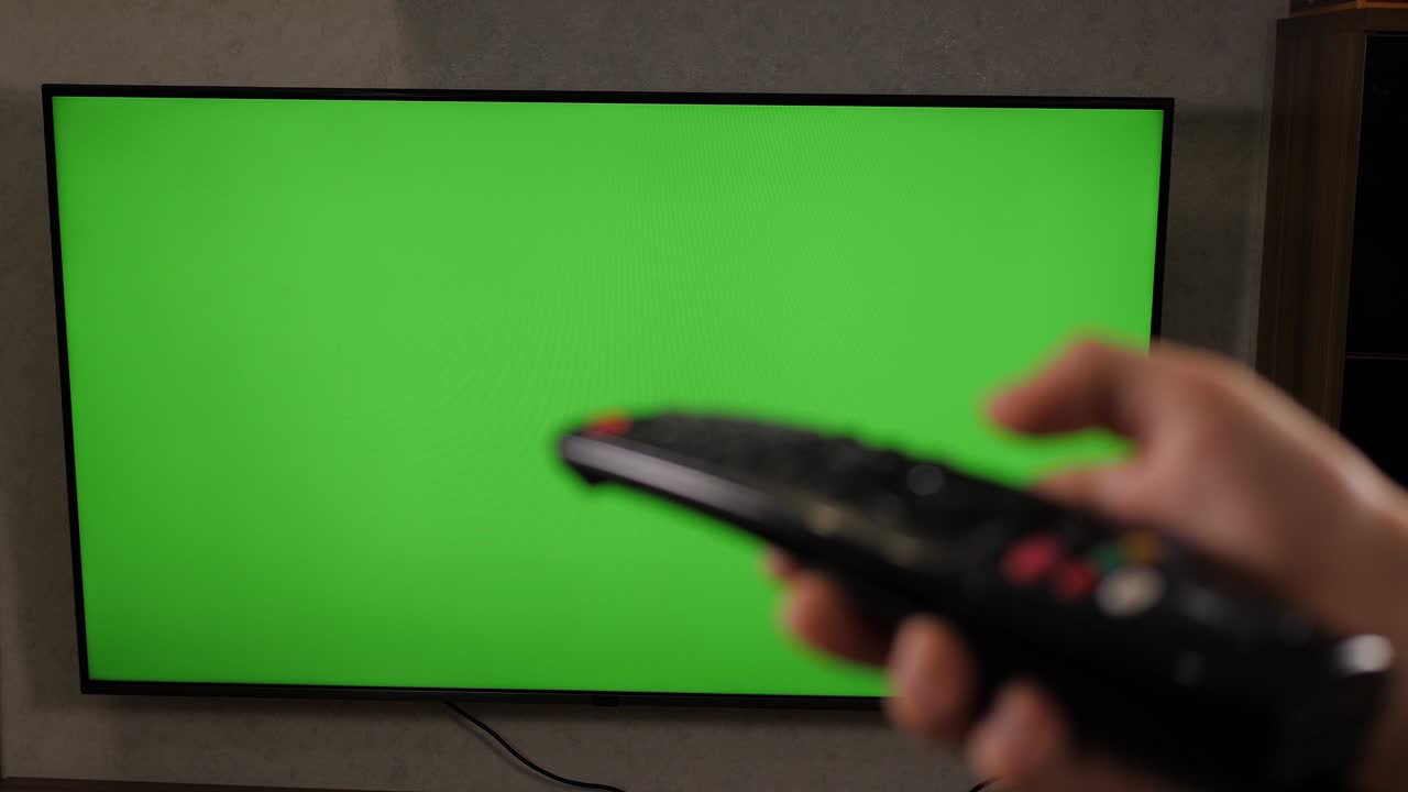 손으로 tv 리모컨을 들고 녹색 화면을 통해 현대적인 텔레비전 세트를 들고 있습니다.