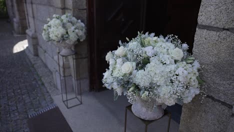 white floral bouquets on pedestals outside a stone building entrance