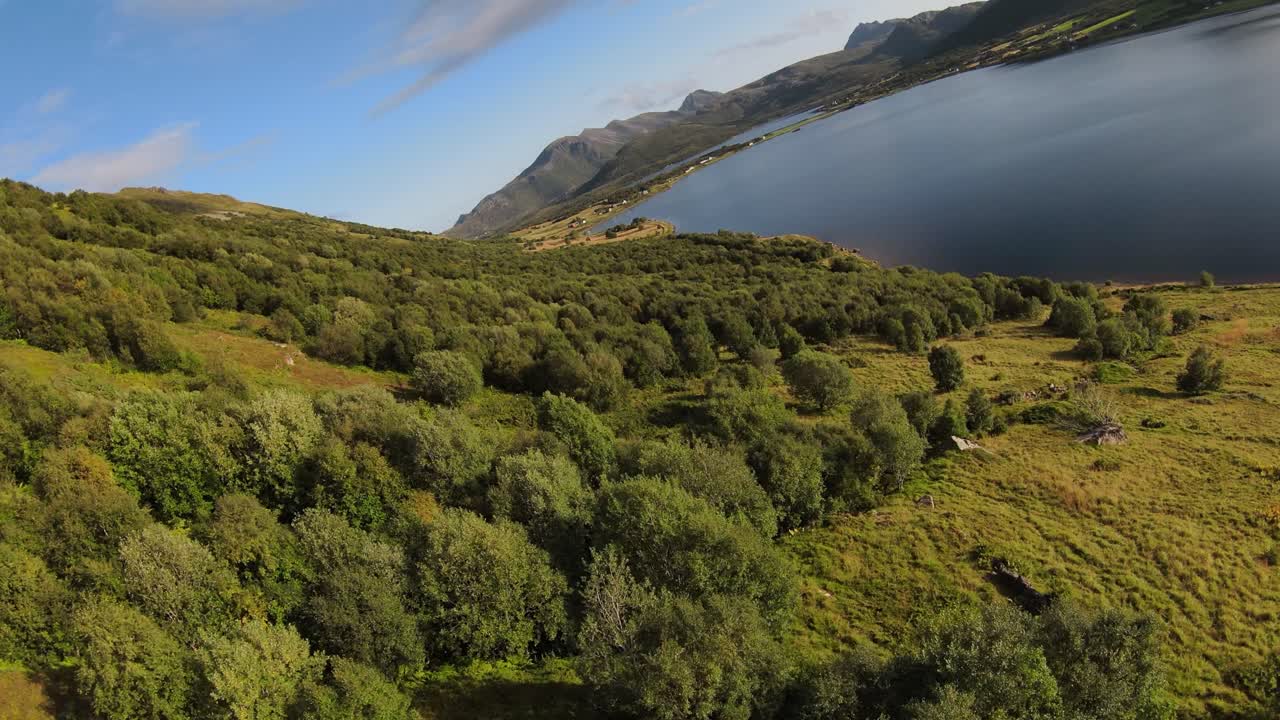 오른쪽으로 호수가 내려다 보이는 산을 따라 비행하고 언덕의 잔디 풍경과 많은 나무