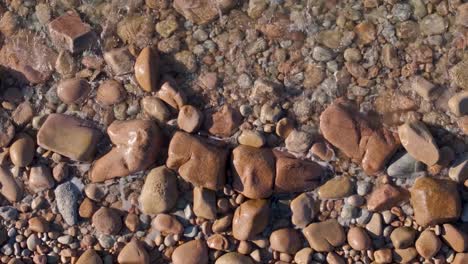 Top-View-Of-A-Stony-Beach-With-Calm-Waves-At-Sunset