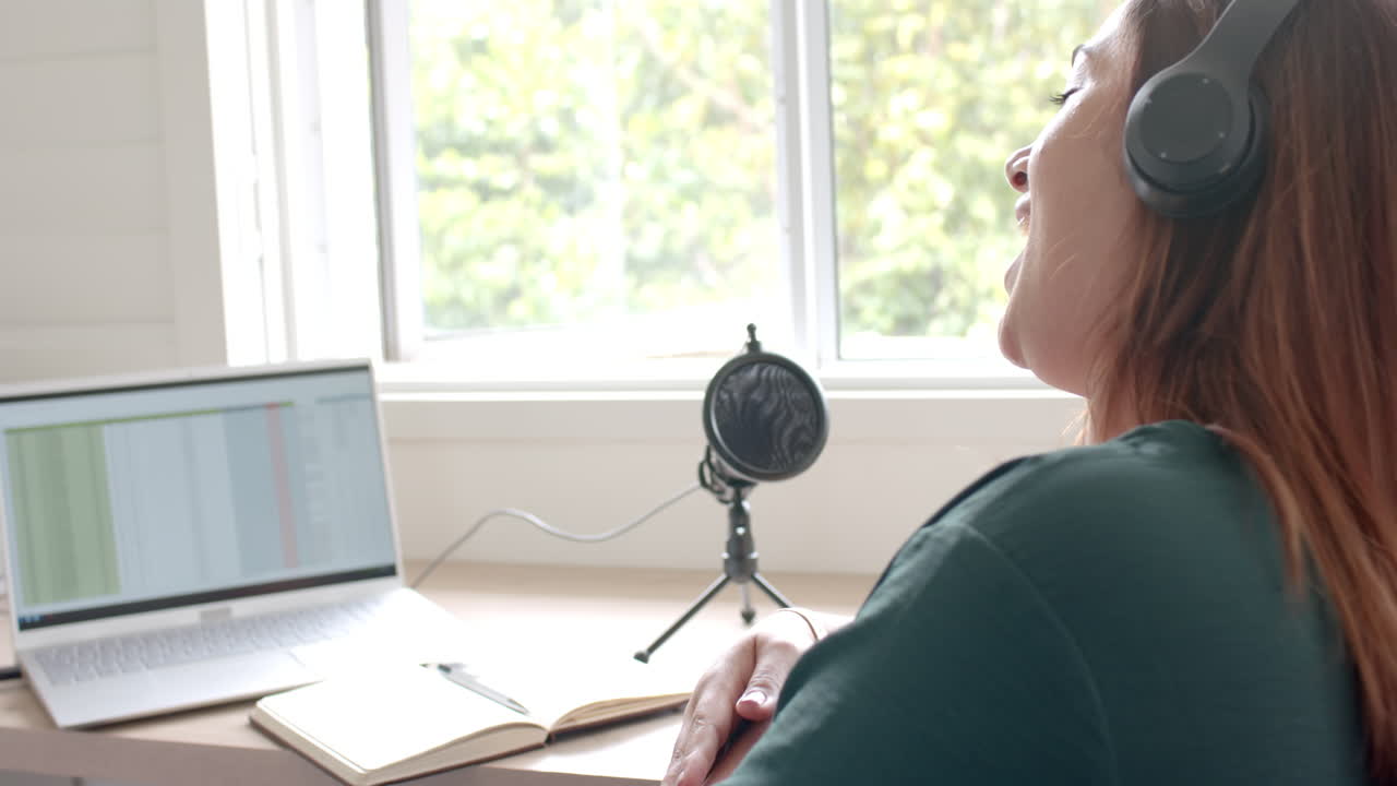 Happy plus size biracial woman in headphones podcasting with laptop at home, copy space, slow motion