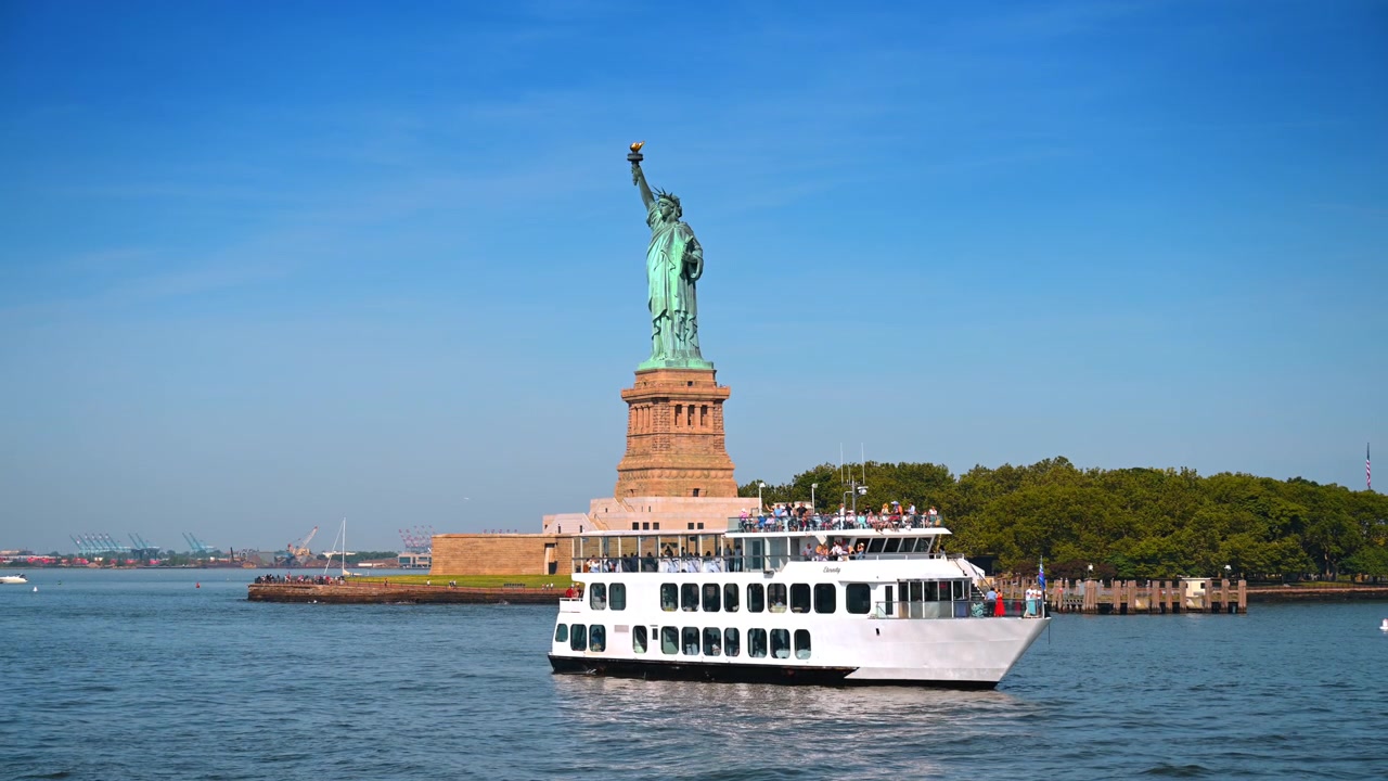 New York, AS, 4 Juli 2026: Kapal wisata melewati Patung Liberty di Pelabuhan New York. Sebuah kapal penumpang putih memenuhi latar depan saat pengunjung berkumpul di dek terbukanya.