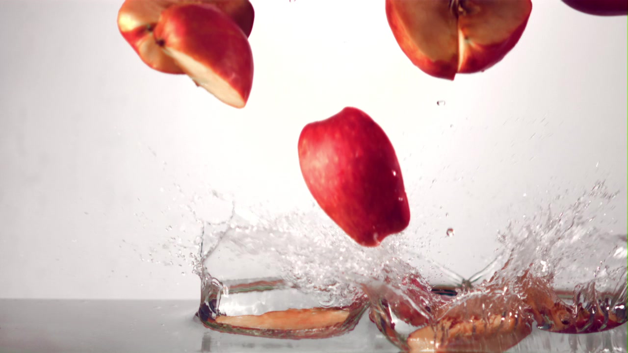 Red Apple Slices and Whole Apple Splashing into Water in Slow Motion