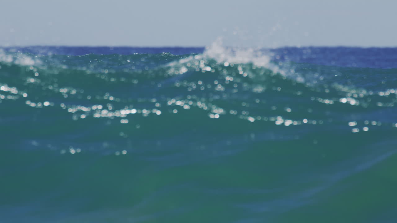 Slow-motion view of a sunrise wave rolling across the ocean surface filmed from inside the water, emphasizing the wave's translucency and motion