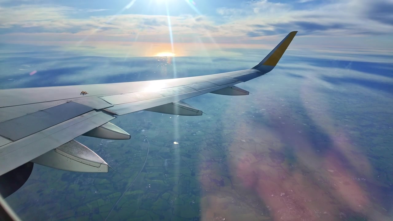 Flyvinge set fra vinduet under flyvning over et landskab med klar sol og skyer