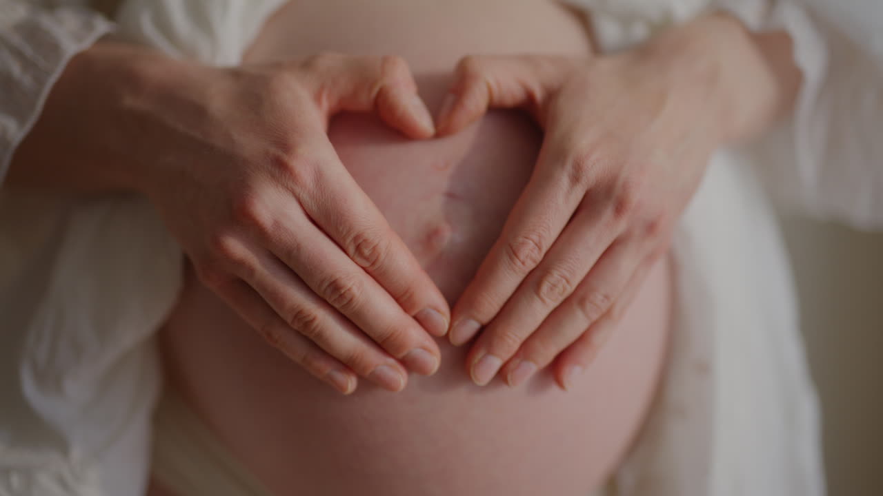 Primo piano della pancia di una donna incinta con le mani a forma di cuore