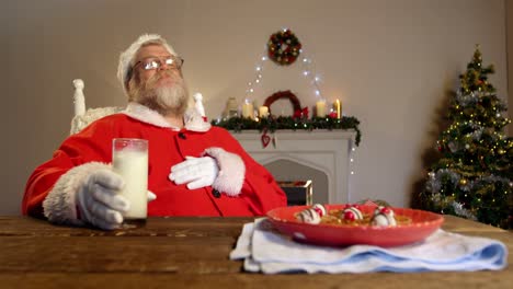 Papá-Noel-Relajándose-En-Una-Silla-Y-Comiendo-Comida-Dulce