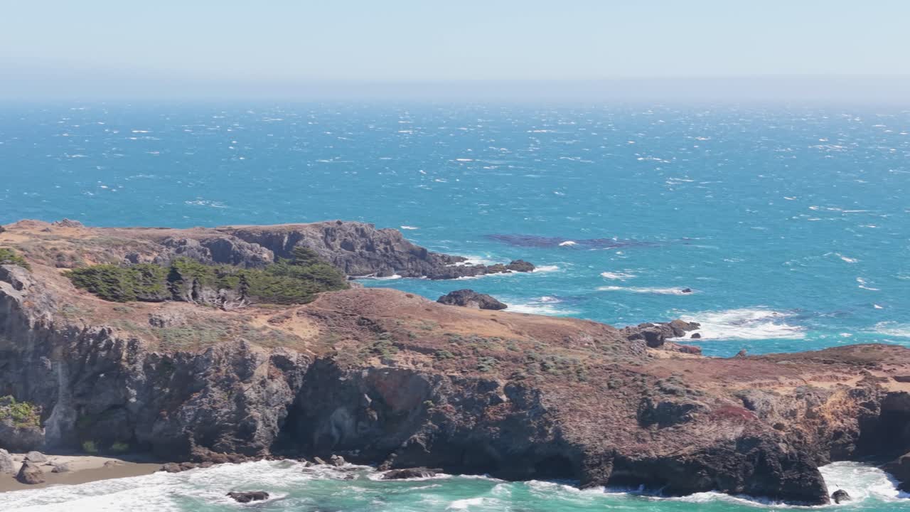Drone captures a high lateral view over cliffs, showing coastal trails, rocky shoreline, and jetty extending into the ocean at Black Point Beach, California