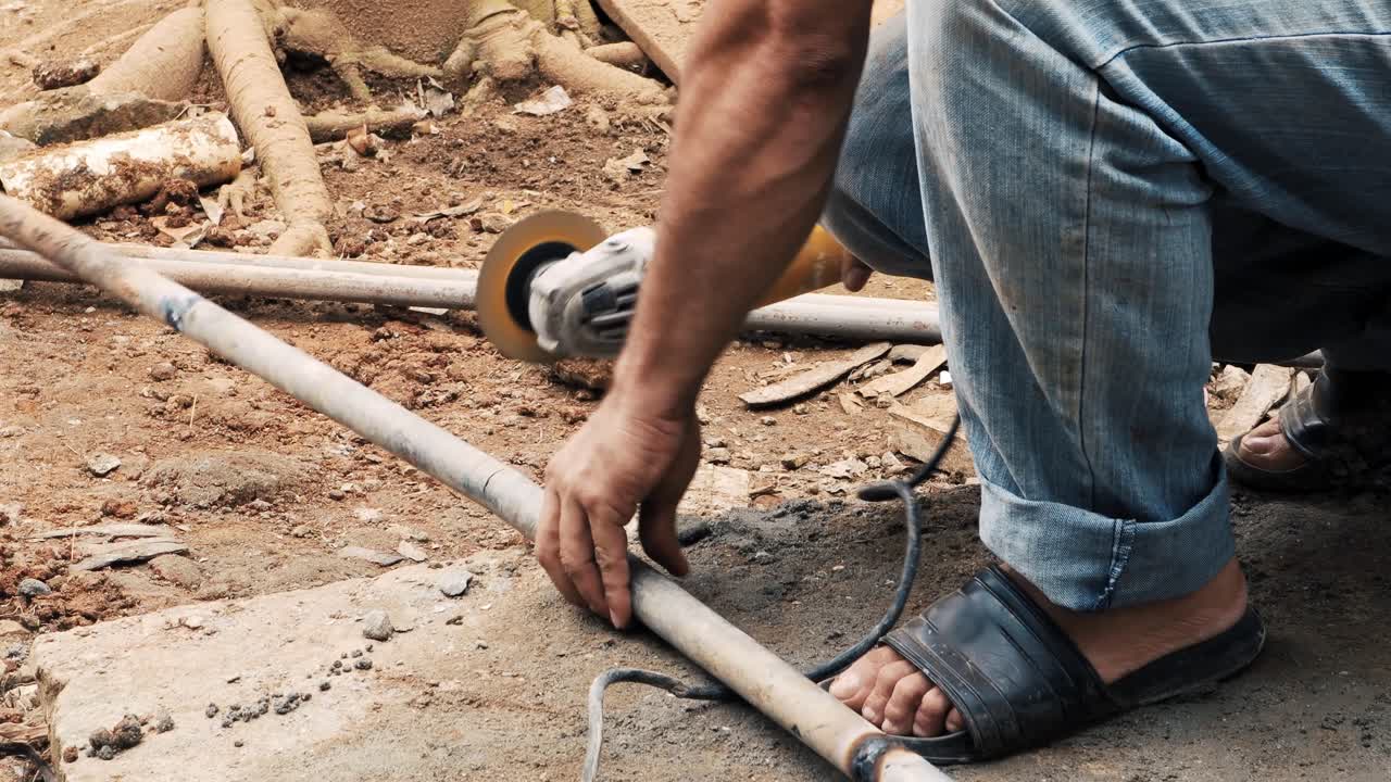 homem cortando um tubo de aço galvanizado com uma rebarbadora elétrica industrial para elaborar uma estrutura metálica em um canteiro de obras em ambiente rural