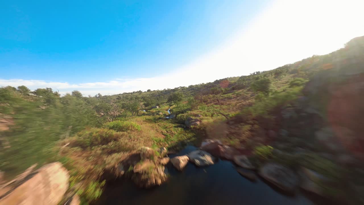 volando a través del rancho de caza de texas siguiendo la corriente a través de la propiedad al atardecer sobre la cascada de los acantilados rocosos a través de los árboles y el campo rural en 4k con un dron fpv