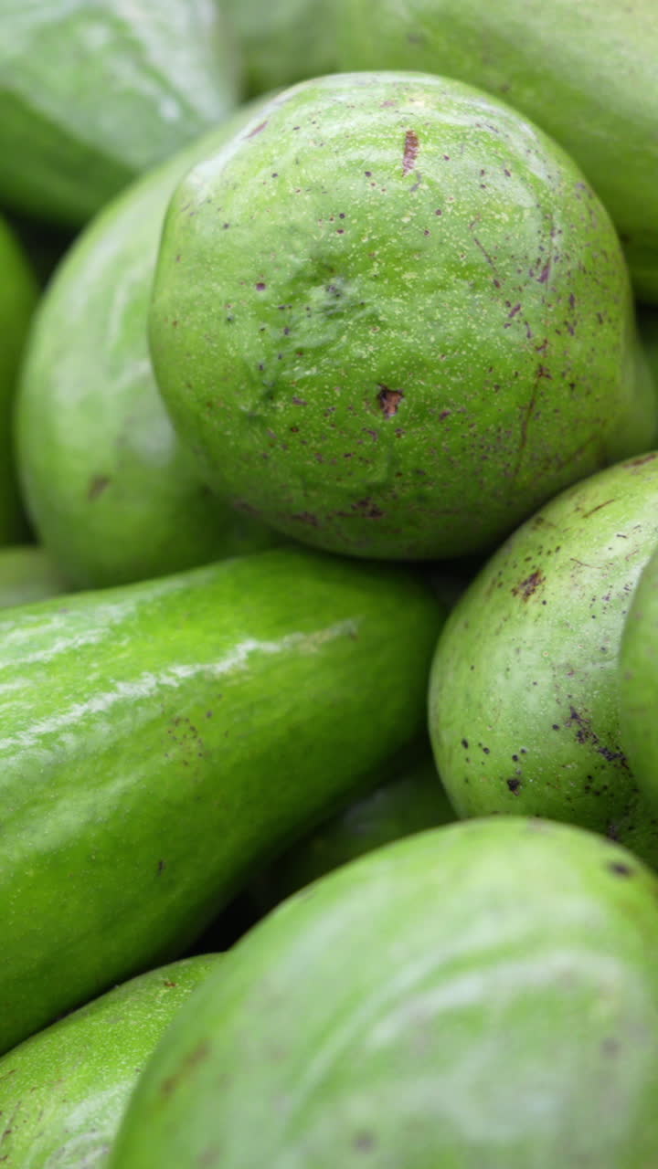 Vibrant close-up of fresh, green avocados piled together, capturing their textured skins and glossy finish. Ideal vertical video for mobile and social media, emphasizing natural produce