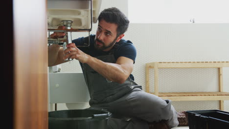 male plumber working to fix leaking sink in home bathroom