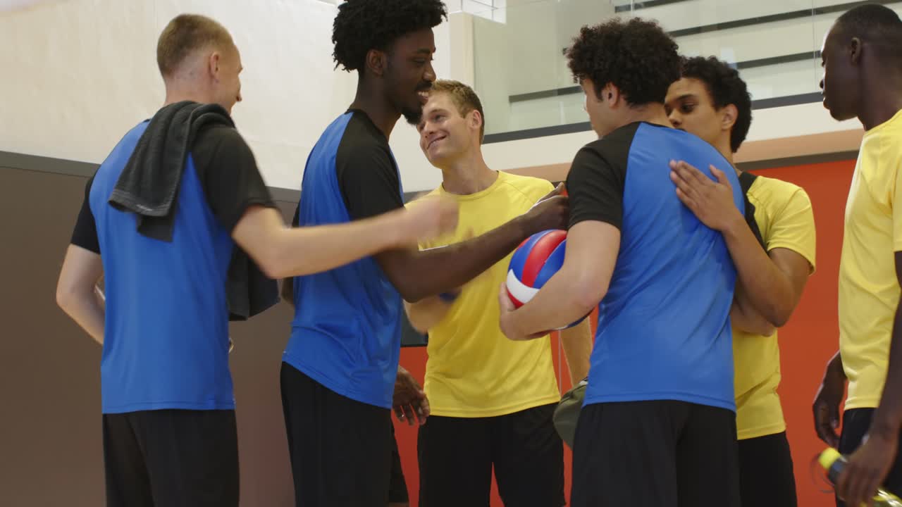 Giocatori di pallavolo uomini di diverse etnie si salutano dopo la partita scambiandosi la palla sul campo, camminando verso porte rosse.