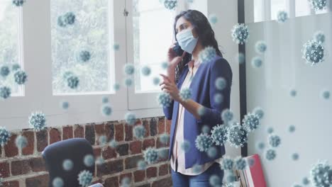 animation of covid 19 cells floating over man wearing face mask, using smartphone in office