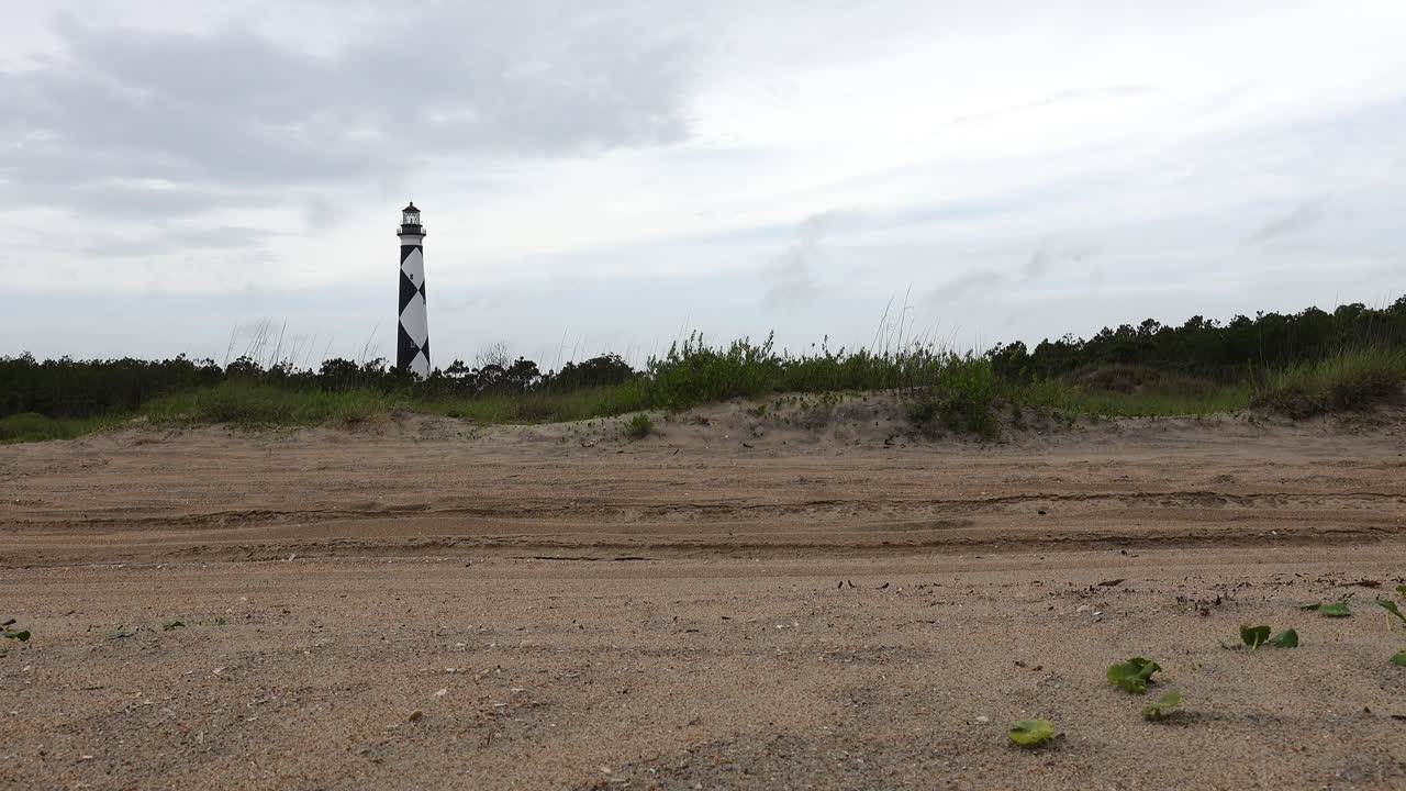 Slow Motion shot of an adventure seeking couple driving their overland vehicle across a beach sand track with a lighthouse in the distance
