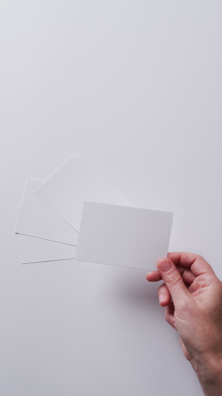 Video verticale di una mano che tiene un pezzo di carta sopra altri fogli con spazio per il testo al rallentatore