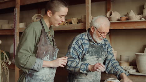 senior potter teaching young female student in workshop