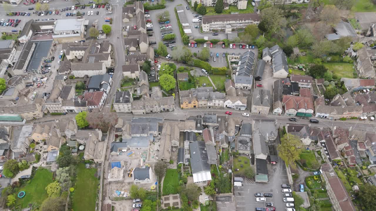 Aerial flyover of traditional small-town high street lined by stone and brick buildings, parked cars and leafy pavements, conveying community life and historic charm
