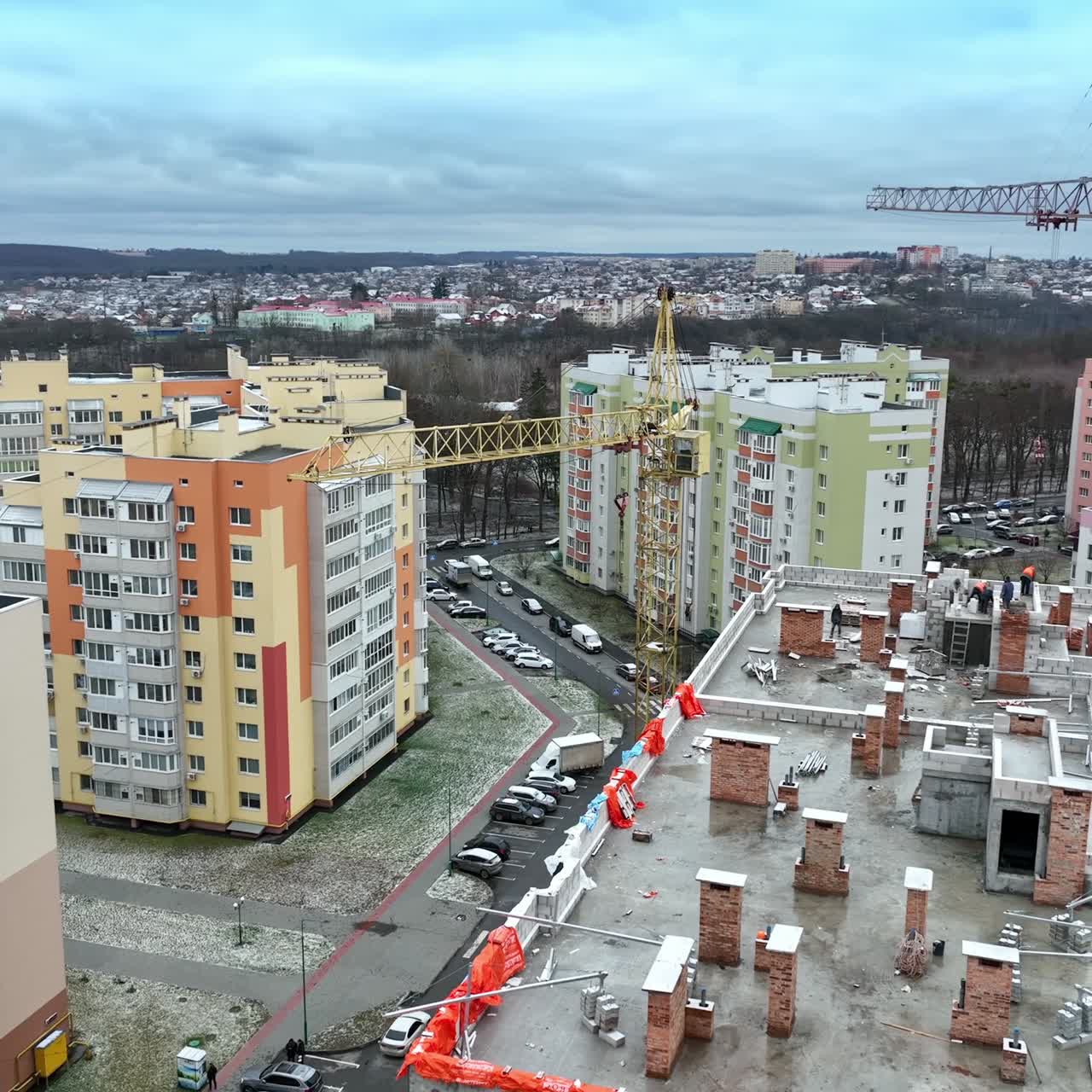Construction cranes towering above the house in construction. Beautiful residential area full of modern apartment blocks. Cityscape at the background