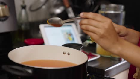 South-asian-woman-putting-spoonful-of-turmeric-in-pot-of-golden-curry