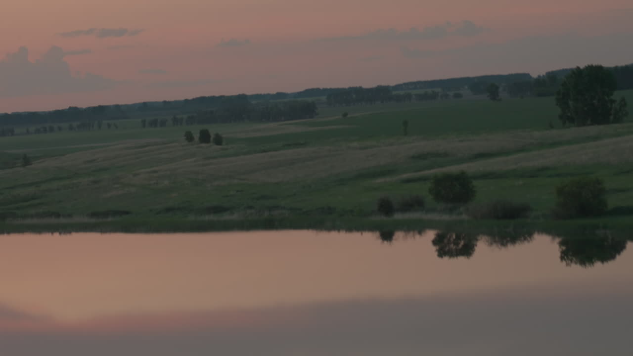 Scenic river winding through serene farmland landscape reflected on calm lake surface at dusk with silhouetted trees framing mirrored sky hues and subtle solar flare