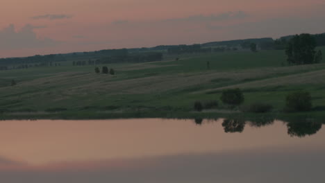 scenic river winding through serene farmland landscape reflected on calm lake surface at dusk with silhouetted trees framing mirrored sky hues and subtle solar flare