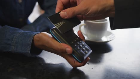 african american woman taking contactless card payment from customer over cafe bar